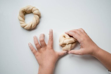 Beyaz yüzey üzerinde elleri ile hamuru örgülü şekillere dönüştüren çocuk.