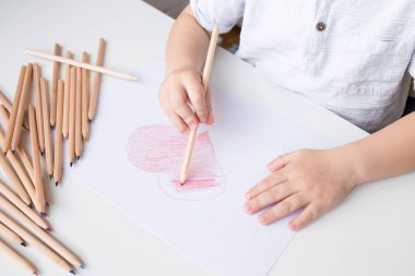 Genç beyaz çocuk kağıda renkli kalemlerle kalp çiziyor..