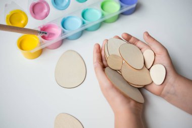Çocuk, yaratıcı işçilik için renkli boya setiyle ahşap Paskalya yumurtaları tutuyor..