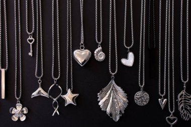 Various silver necklaces and pendants on black background.