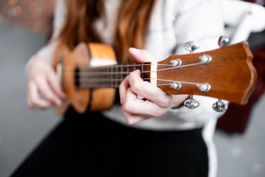 İçerde gitar çalan genç bir kadın. Tellere ve ellere odaklanmış..
