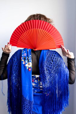 Geleneksel mavi şallı İspanyol kadın kırmızı yelpaze tutuyor..