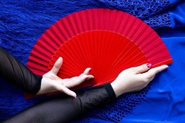 Mavi kumaş arka planda kırmızı yelpaze tutan zarif bir el..