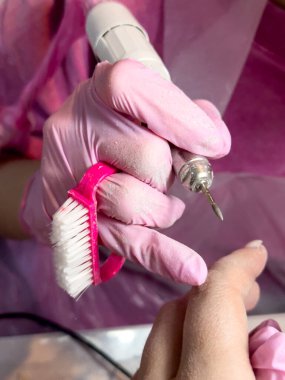 Profesyonel manikür işlemi. Pembe eldivenler ve müşteri elinde tırnak matkabı..