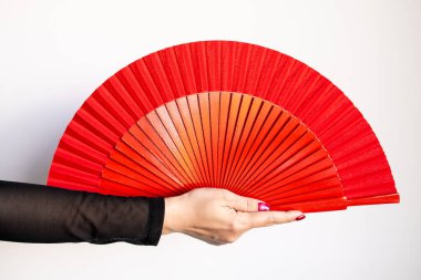 Beyaz arka plana karşı büyük kırmızı yelpaze tutan beyaz kadın eli..