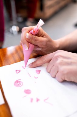 Boru torbası kullanarak kağıt üzerine pembe krema ile el dekorasyonu..