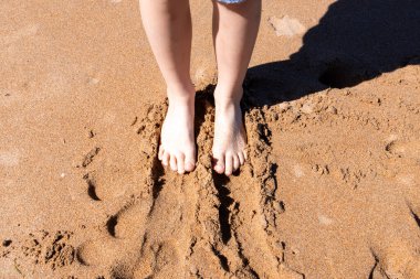 Kumlu sahilde gün ışığında genç beyaz bir kadının ayakları..