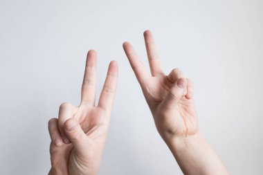 Beyaz eller ışık arka planına karşı barış işareti gösteriyorlar.