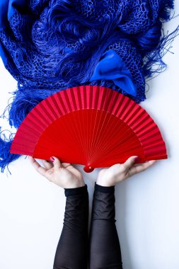 Mavi tekstil sergilenen kırmızı yelpaze tutan kadın elleri.