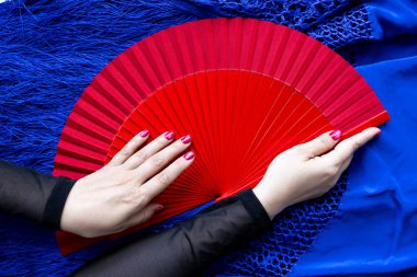 Kırmızı yelpazeyi kapat ve beyaz kadın ellerini mavi kumaşın üzerinde tut..