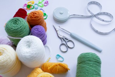 Beyaz yüzeyde renkli iplik topları ve tığ işi araçları.