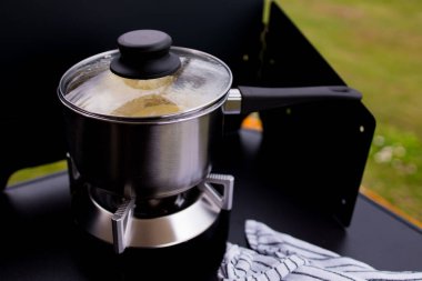 Dışarıda cam kapaklı taşınabilir sobanın üzerinde paslanmaz çelik tencere..