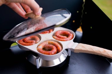 Portatif ızgarada ahşap saplı ve dairesel tavalı sosis pişirmek..