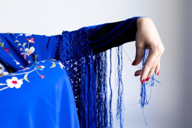 Beyaz kadın eli, çiçekli, mavi püsküllü şalla örtülmüş..