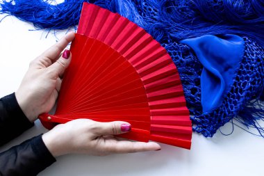 Kırmızı el yelpaze, mavi örgü ve püsküllü beyaz kadın tarafından tutuluyor..