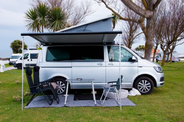 Kamp minibüsü, tenteli ve sandalyeli manzaralı kamp alanında..