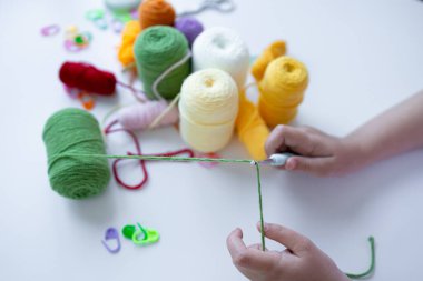 Beyaz yüzeyde renkli ipliklerle tığ işi yapan çocuk..