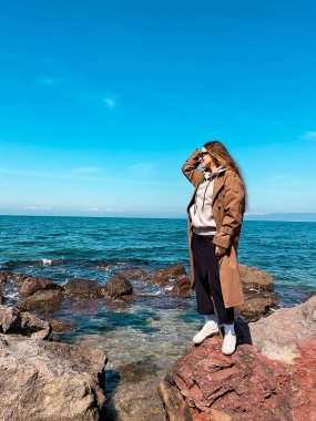 Genç beyaz kadın açık mavi gökyüzünün altında kayalık kıyılarda manzaranın tadını çıkarıyor..