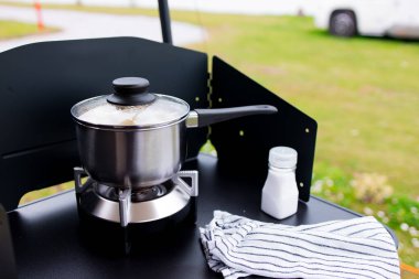 Portatif sobada demlik ve siyah yüzeyde tuzluk olan açık hava yemek sahnesi..