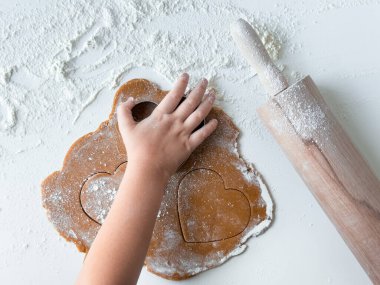 Un kaplı yüzeyde merdaneyle kalp şeklinde kurabiyeler yapan çocuk..