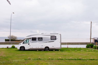 Bulutlu bir günde deniz kenarına park edilmiş modern bir karavan..