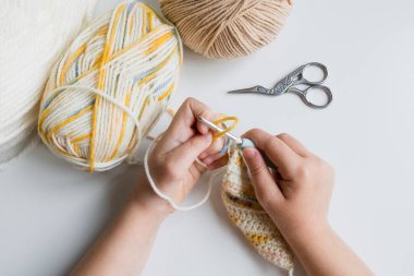 Beyaz masada makas ve iplikle tığ işi yapan çocuk..