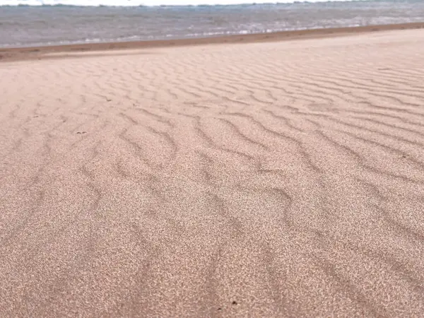 Sakin bir sahil şeridinde dalgalı kum desenleri.