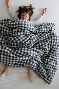 Genç beyaz kadın çocuk kareli yatakta rahat bir şekilde uyuyor..