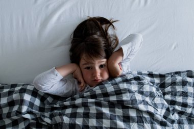 Kafkasyalı genç kız elleri kulaklarında kareli battaniyenin altında dinleniyor..