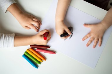 Beyaz kağıt yüzeyine renkli boya kalemleri çizen çocuklar.