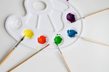 Beyaz arkaplanda fırçalar ve canlı akrilik renkler ile renkli boya paleti.