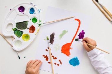 Çocuk, soyut sanat eserlerini renkli paletler ve beyaz kağıda fırçalar ile boyuyor..