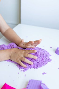 Beyaz masada mor kinetik kumla oynayan bir çocuk. Yüksek kalite.