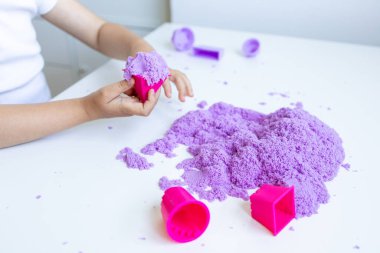 Beyaz masada mor kinetik kum ve pembe kalıplarla oynayan bir çocuk. Yüksek kalite.