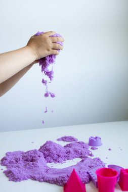 Beyaz yüzeyde mor kinetik kumla oynayan bir çocuk. Yüksek kalite.