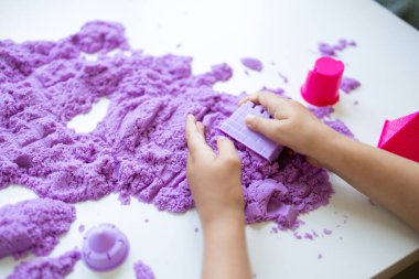 Beyaz bir masada mor kinetik kum ve kalıplarla oynayan bir çocuk. Yüksek kalite.