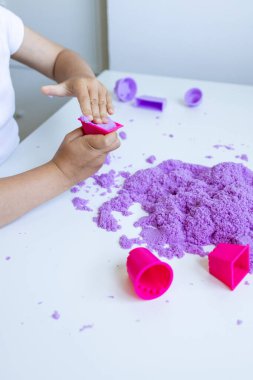 Beyaz masada mor kinetik kumla oynayan bir çocuk. Yüksek kalite.