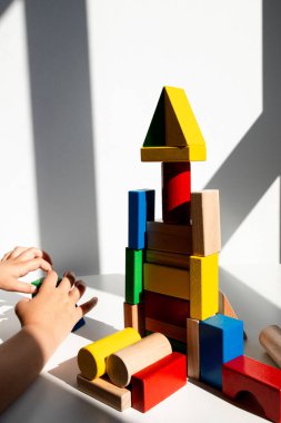 Güneşli odada renkli ahşap yapı taşlarıyla oynayan bir çocuk. Yüksek kalite.