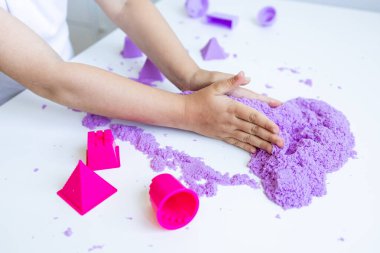 Çocuk, mor kinetik kumla ve beyaz masada şekillenmiş şekillerle oynuyor. Yüksek kalite.