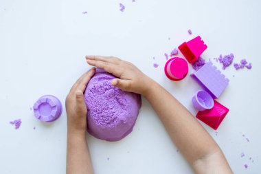 Çocuk elleri mor kinetik kumu beyaz arka planda renkli kalıplarla şekillendiriyor. Yüksek kalite.
