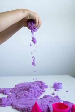 Beyaz yüzeyde mor kinetik kumla oynayan bir çocuk. Yüksek kalite.