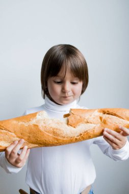 Beyaz gömlekli, arka planda beyaz ekmek tutan beyaz bir çocuk..