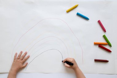 Kağıda pastel boyalarla renkli gökkuşağı çizen çocuk.