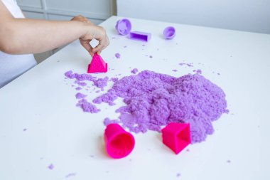Beyaz masada mor kum ve küflerle oynayan çocuk eli. Yüksek kalite.