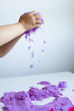Beyaz masada mor kinetik kumla oynayan bir çocuk. Yüksek kalite.