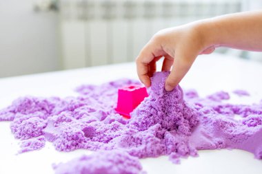 Çocuk eli masada mor kinetik kum ve pembe küfle oynuyor. Yüksek kalite.