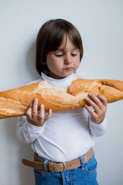 Beyaz duvara baget tutan uzun kahverengi saçlı beyaz bir çocuk..