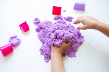 Beyaz arka planda mor kinetik kum ve plastik oyuncak şekilleriyle oynayan bir çocuk. Yüksek kalite.