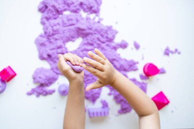 Beyaz arka planda mor kinetik kum ve küflerle oynayan çocuk elleri. Yüksek kalite.