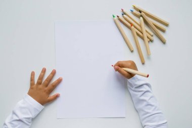 Beyaz arkaplanda renkli kalemlerle boş kağıda resim çizen çocuk.